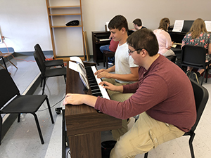 Male students practicing the piano in the music appreciation class